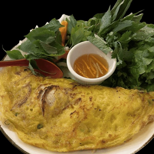 A Vietnamese savory crepe (Banh Xeo) with fresh herbs and a dipping sauce.